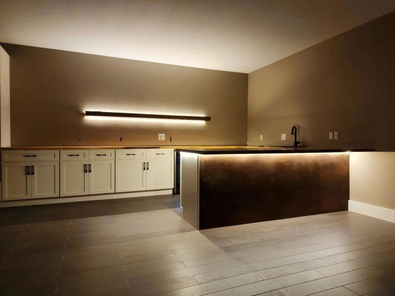 A basement bar with white cabinets and lit shelving