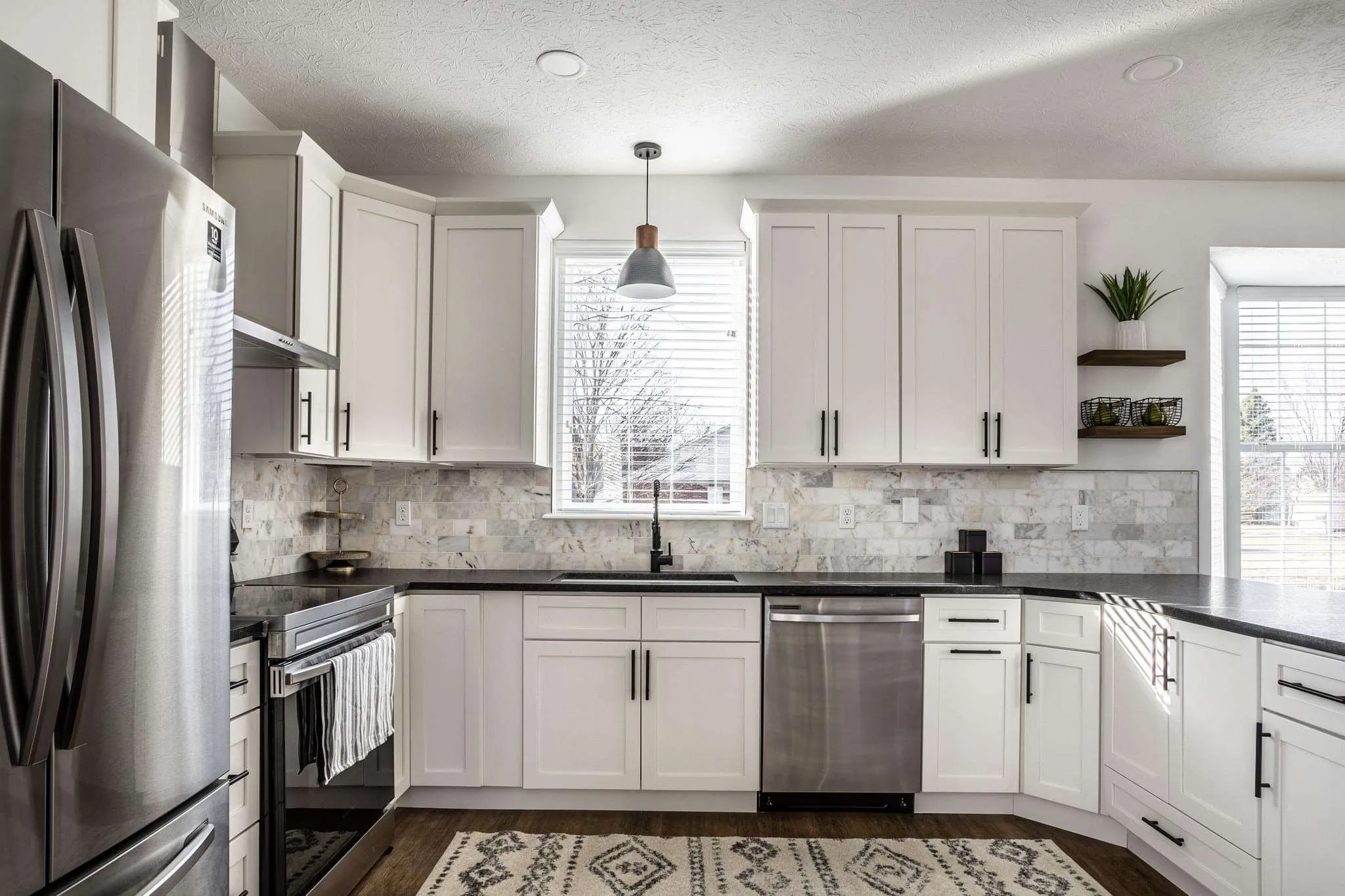 Kitchen finished with white shaker cabinets, marble backsplash and black hardware, built with Cascade Cabinets in Fort Wayne