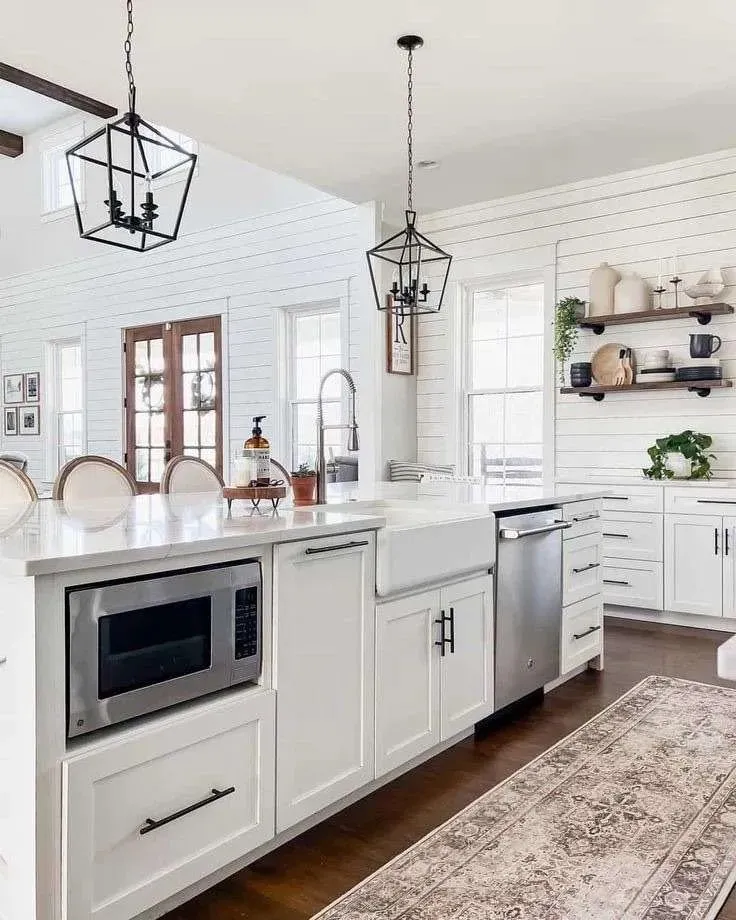 A white kitchen with a marble island, farmhouse sink and open shelving